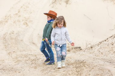elinde silah olan bir Şerif şapkalı çocuk bir kız ile yürüyor