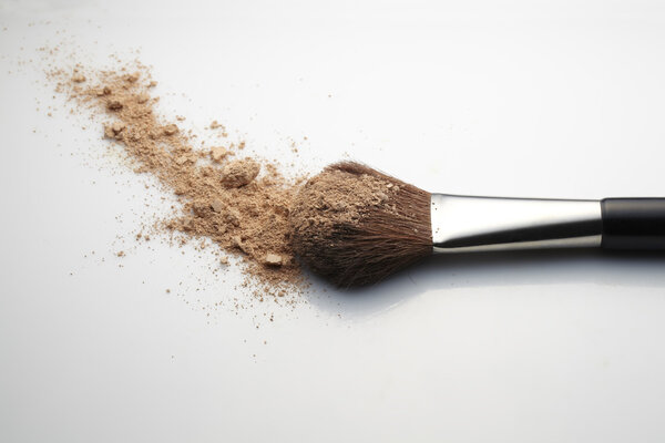 Makeup Brush with beige loose Face Powder placed horizontal on white gradient background