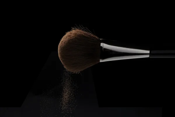 Horizontal closeup photo of makeup brush with beige powder in motion isolated on black background. — Stock Photo, Image