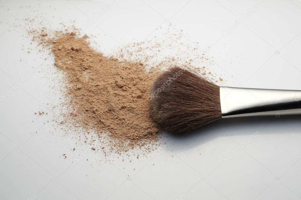 Makeup Brush with beige loose Face Powder placed horizontal on white gradient background