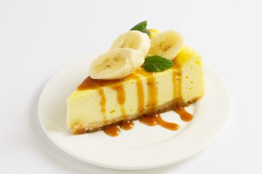 Karamel sosu, muz ve nane plaka üzerinde beyaz masa üzerinde dilim cheesecake tepesinde, yakın çekim