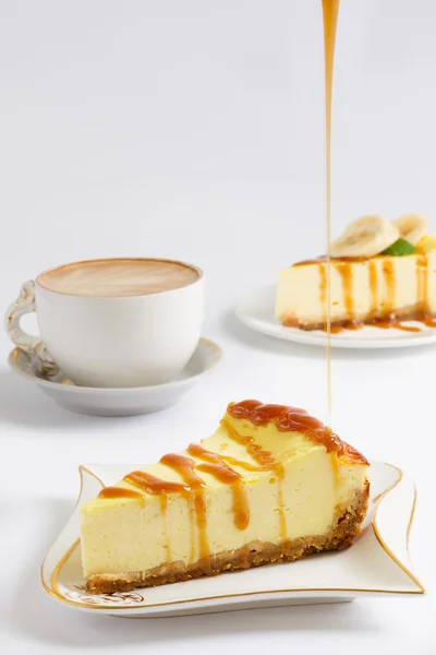 Scheibe Käsekuchen gießen einen dünnen Strom von Karamellsoße, Tasse Kaffee auf dem weißen Hintergrund — Stockfoto