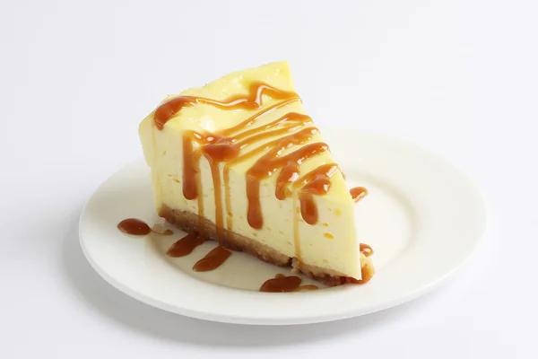 Slice of cheesecake topped with caramel sauce on plate on white table, close up — Stock Photo, Image