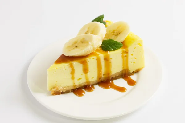 Fetta di cheesecake condita con salsa al caramello, banana e menta sul piatto sul tavolo bianco, da vicino — Foto Stock