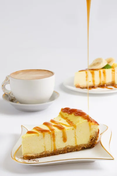 チーズケーキのスライスをキャラメル ソース、白い背景の上のコーヒー カップの薄い流れを注ぐ ロイヤリティフリーのストック画像