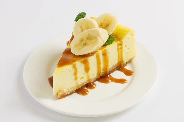 チーズケーキのスライスは、キャラメル ソース、バナナ、白いテーブルの上皿にミントをトッピング、クローズ アップ ストック画像