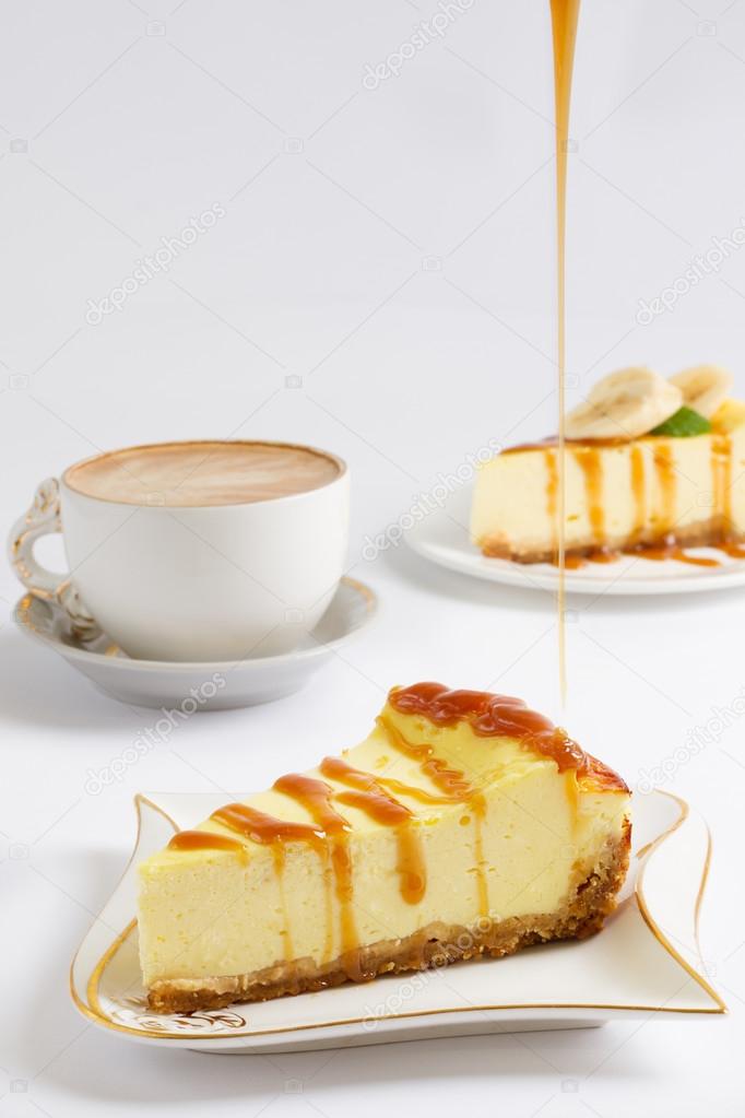 Slice of cheesecake pour a thin stream of caramel sauce, cup of coffee on the white background