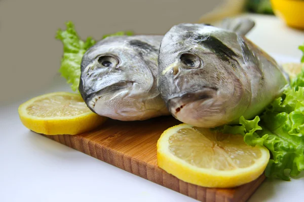 Dorado fresco en tabla de cortar con limón y verduras —  Fotos de Stock