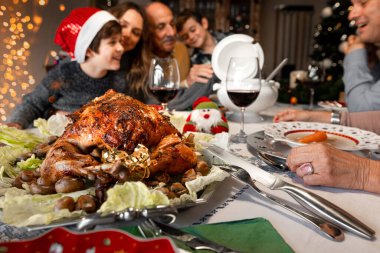 Güzel dekore edilmiş bir Noel masasında, etrafında mutlu bir gülümseme ailesi olan lezzetli bir hindinin kapağını kapatın. Birlikte olmayı kutluyoruz, yemek ve içkiler, Noel tatili..