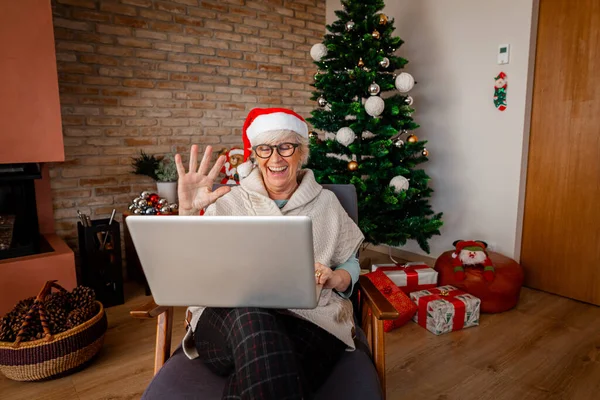 自宅で幸せな笑いのシニア女性は コンピュータのビデオ通話や手を自宅で手を振っている クリスマス オンライン通信 社会的距離 自己隔離 隔離概念 — ストック写真