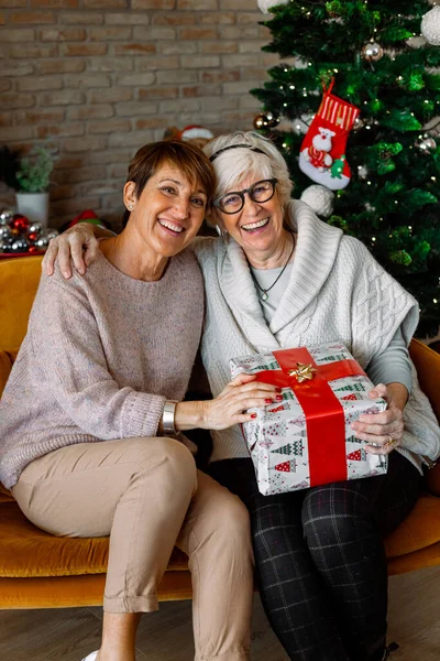 Ältere Freundinnen Tauschen Weihnachtsgeschenke Aus Lächeln Und Blicken Die Kamera — Stockfoto