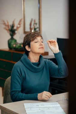 Yaşlı kadının portresi oturuyor, antijen kiti ile evde COVID-19 testi yapıyor. Muhtemel Coronavirus enfeksiyonu için burun temizleme testi. İnternet üzerinden tıp ve sağlıkla ilgili hizmetler.