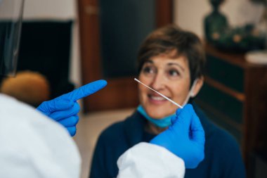 Close up of the nasal swab used by a health Professional to test for Covid-19 a senior patient on a home visit.Doctor protected with gloves and PPE suit. Rapid Antigen Test during Coronavirus Pandemic clipart
