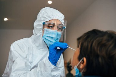 Close up of female health Professional in PPE introducing a nasal swab to a senior female patient at her house. Rapid Antigen Test kit to analyze nasal culture sampling while coronavirus Pandemic. clipart