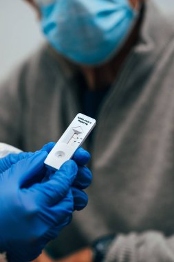 SARS Covid-19 için negatif antijen testinin incelenmesi. Yeni Coronavirus enfeksiyonu için burun kültürü örnekleme ve test cihazı kullanarak hızlı bir test. Eldivenli, PPE kostümlü ve kıdemli bir hasta..
