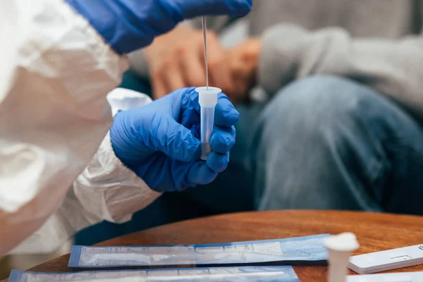 Close up of medical staff hands introducing the nasal swab to the buffer tube to take a nasal culture sampling from a senior man at his home, on a home visit. Rapid Antigen Test for Covid-19.