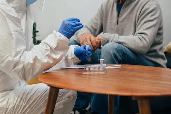 Close up of medical staff hands introducing the nasal swab to the buffer tube to take a nasal culture sampling from a senior man at his home, on a home visit. Rapid Antigen Test for Covid-19.