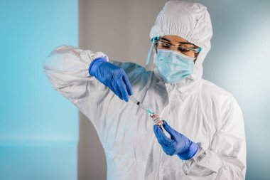 PPE giysisi, maske ve eldiven giyen laboratuvar araştırmacısı şırıngaya COVID-19 aşı sıvısı çekiyor. Koronavirüs salgınıyla savaşıyorum. Coronavirus aşılama kampanyası başladı..