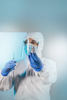 Araştırmacıların elinde COVID-19 aşısı, kadın doktor Coronavirus tedavisi aşısı için şırınga ve şişe tutuyor. Salgın sırasında korona virüsü tedavisi, enjeksiyon, iğne ve klinik deney kavramı.