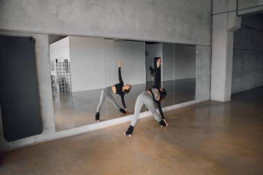 Fit kadın yoga eğitmeni, esnerken bir spor salonunun aynasına yansıyor. Büyük bir endüstriyel spor salonunda pilates yapan bir kadın. Düşük ihtimal.