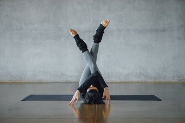 Genç kadın antrenör beyaz arka planda siyah bir minder üzerinde bireysel hatha yogası yapıyor, pilates stüdyosu. Spor kıyafetleri giyip, içeride. Yatay