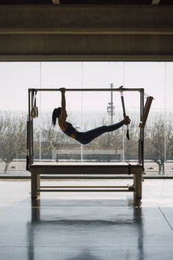 Pilates makinesinden sallanan kadın eğitmen, büyük pencereli ve sokak manzaralı büyük bir spor salonundaki Trapez Masası 'nda çalışan kadın. İçeride, gündüz vakti..