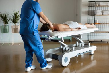 Modern tıp merkezinde profesyonel masör ya da fizyoterapist tarafından yapılan vücut masajından zevk alan rahat ve sırtüstü genç bir kadının uzun pozu. Servikal omurga için Osteopatik elle tedavi.