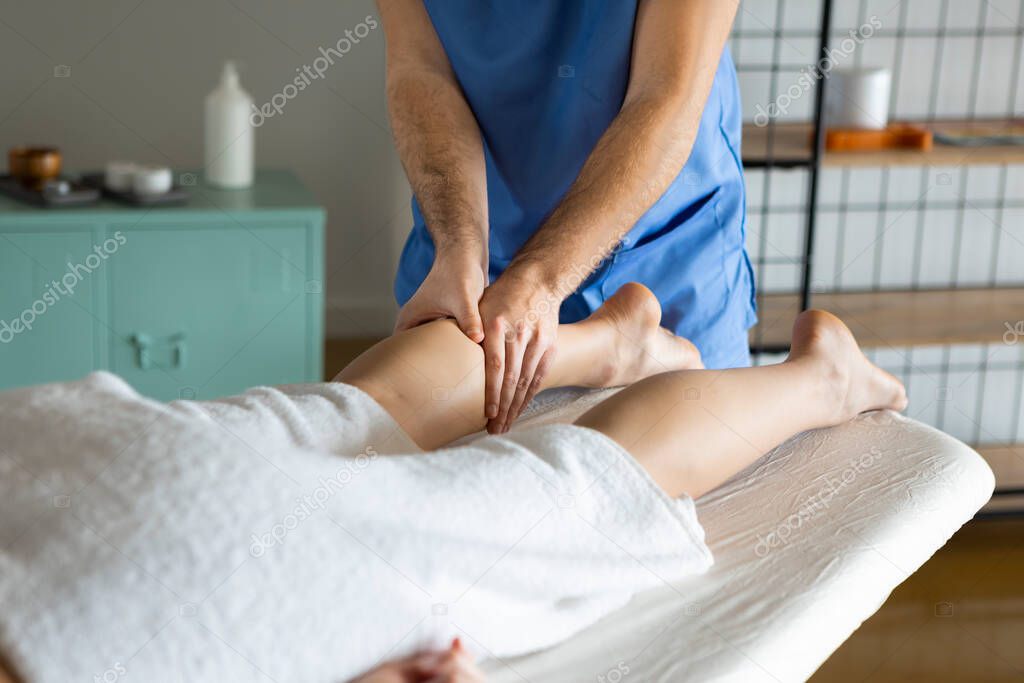 Lymphatic drainage massage of legs and lower legs. Close up of Female feet in the hands of a professional medical masseur or physiotherapist giving a manual therapy in a health and beauty center.
