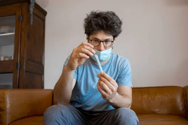 Young man sitting at living room at home manipulating Antigen kit test tube after performing Self-swabbing home tests for COVID-19. Hands holding testing equipment for Coronavirus diagnostic.