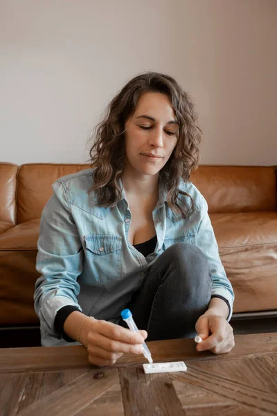 Young woman sitting at living room at home manipulating Antigen kit test tube after performing Self-swabbing home tests for COVID-19. Hands holding testing equipment for Coronavirus diagnostic.