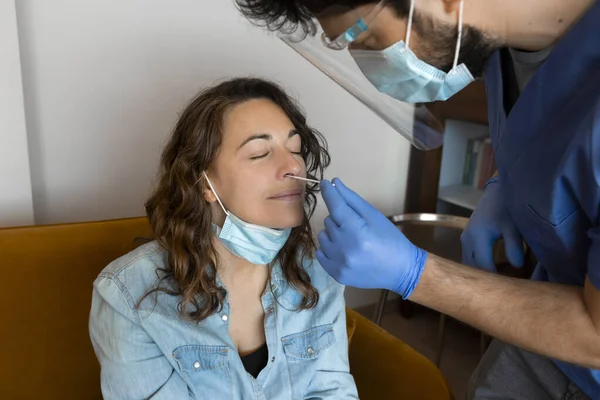 Home medical visit during Coronavirus Pandemic. Doctor or nurse in gloves, protective mask and Face shield protector, testing for Covid-19 with a nasal swab a young woman. Antigen Test.