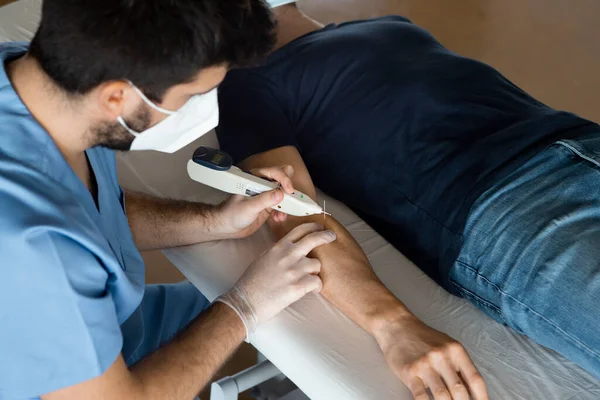 Top angle of man lying down on a stretcher of a health center, receiving a alternative treatment, Electroacupuncture dry with needle for arm injury with electric shock device, done by physiotherapist.