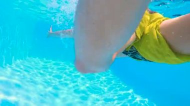Yavaş hareket et, UNDERWATER, KUŞAĞI KUŞAĞI: Sarı mayo giyen çocuk sıcak güneşli bir günde güneşlenmek için mavi berrak havuza dalıyor, kabarcıklar ve güneş ışığı ile. Çocuk yaz tatilinin tadını çıkarıyor.