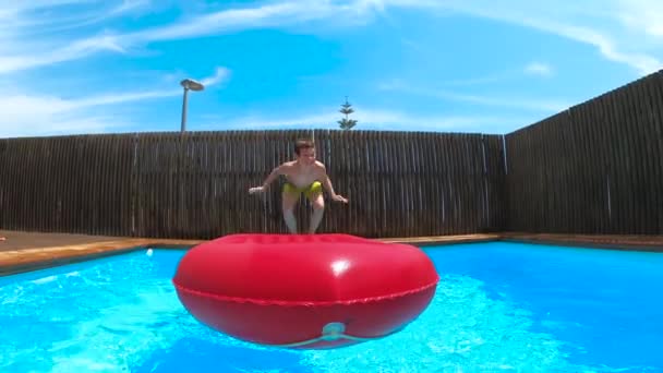 ゆっくりとした動き 幅の広い角度 コーカサスの少年は 開いている腕と足で赤い浮きボートのスイミングプールにジャンプします 晴れた日の夏休みに遊ぶ子供 — ストック動画