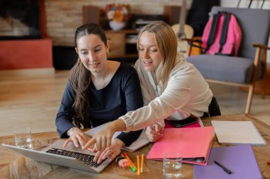 İki kız öğrenci ödevlerini dizüstü bilgisayarla, defterlerle ve dosyalarla ahşap bir masada yapıyor. Öğrenme, takım çalışması, destek ve verimlilik kavramı. Kapalı yatay yakın plan görüntü.