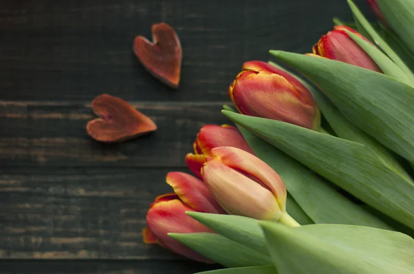 二つの心と暗い木製の板にチューリップの花束 — ストック写真