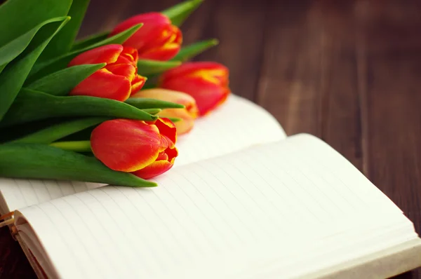 Ramo de tulipanes y cuaderno abierto en blanco sobre tablones de madera oscura . —  Fotos de Stock