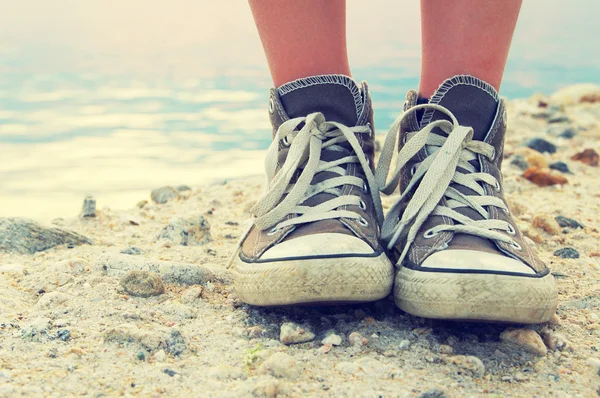 Bijhouden van de voeten van het kind van de tiener in gym schoenen op steen tegen de zee. — Stockfoto