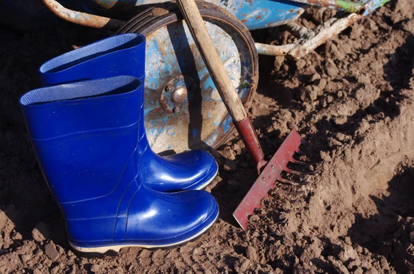 Rastrillo, botas de goma y carro en el campo. Preparación para los trabajos sobre el terreno . — Foto de Stock