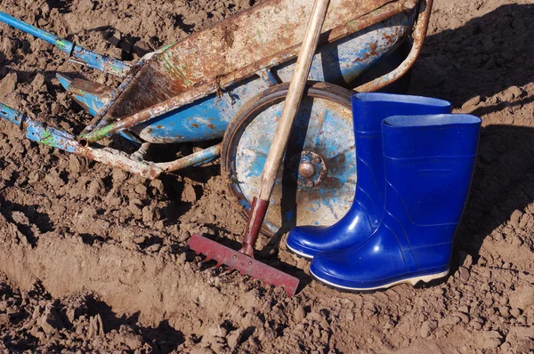 Hark, gumboots en kar in het veld. Voorbereiding op werk op het gebied. — Stockfoto