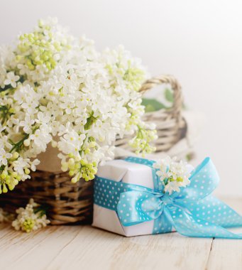 Bir sepet ve bir ahşap yüzeyde bir hediye kutusu beyaz leylak buket.