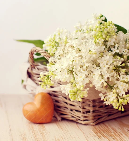 Bir sepet ve kalp bir ahşap yüzeyde taşlarla beyaz leylak buket. 