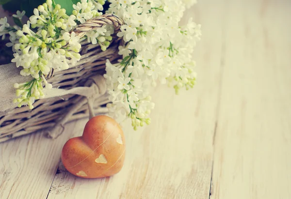 Bouquet of a white lilac in a basket and heart with stones on a wooden surface. — Stock Photo, Image