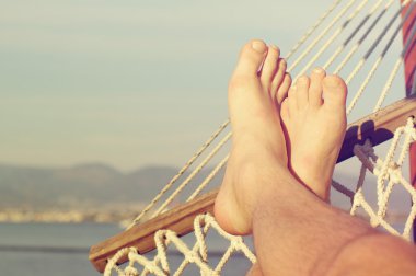 Güneşli bir yaz denize karşı sahilde bir hamakta erkek bacaklar. 