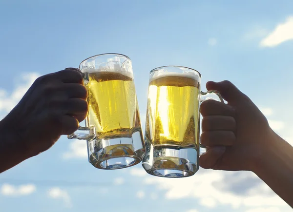 Дві склянки легкого пива тримають чоловічі руки на тлі блакитного неба. Друзі тости з пшеничним пивом — стокове фото