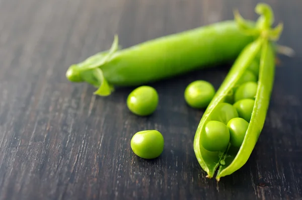 Vainas de guisantes verdes y guisantes en una superficie de madera oscura —  Fotos de Stock