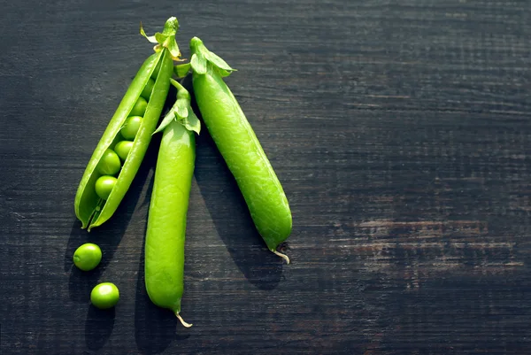 Vainas de guisantes verdes y guisantes en una superficie de madera oscura —  Fotos de Stock