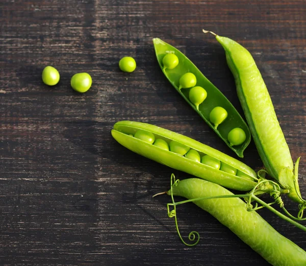 Des gousses de pois verts et de pois sur une surface en bois sombre — Photo