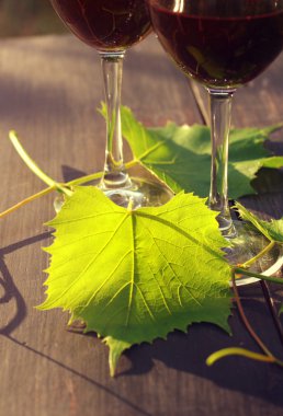 İki kadeh kırmızı şarap ve üzüm yaprakları bir ahşap yüzeye