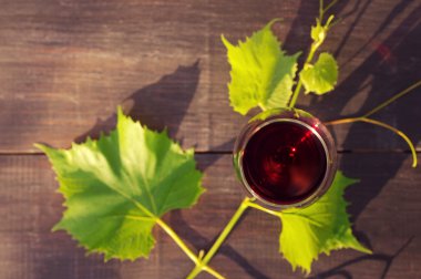 Bir ahşap yüzeye kadeh kırmızı şarap ve üzüm yaprakları